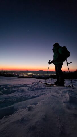 Daniel Tamaki, guia no Japão, com equipamento de esqui sobre a neve em um pôr do sol, representando a experiência de esqui e snowboard no Japão. Ideal para quem busca um guia para esportes de inverno em montanhas japonesas.